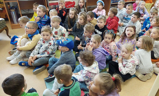 Duża grupa dzieci siedzi na dywanie w bibliotece w Zblewie